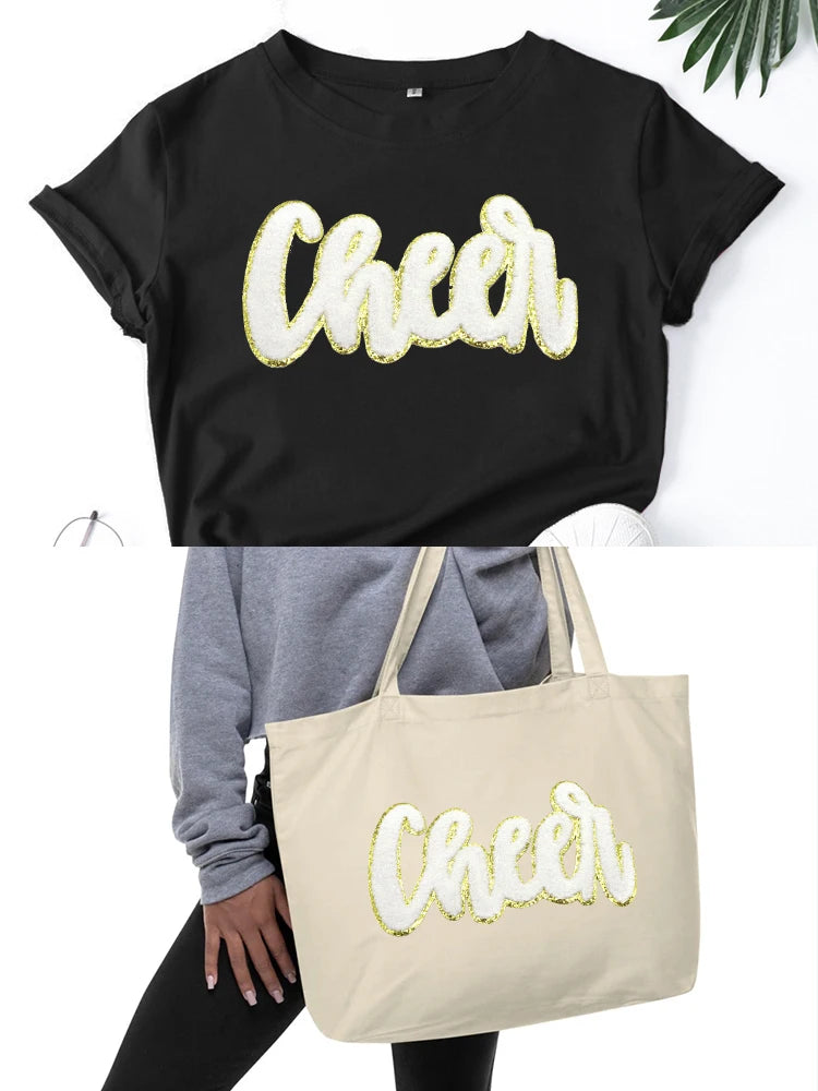 Black t-shirt with a gold glitter cheer letter patch on the chest and a beige canvas tote bag.