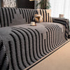 A gray woven throw blanket with black stripes is draped over a sofa, next to a potted plant and a small mug.