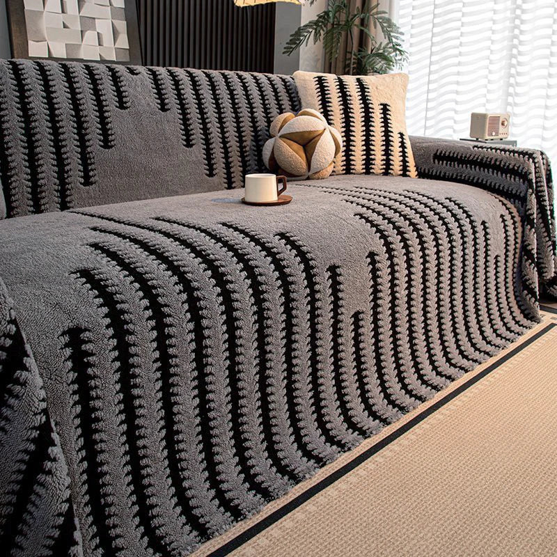 A gray woven throw blanket with black stripes is draped over a sofa, next to a potted plant and a small mug.