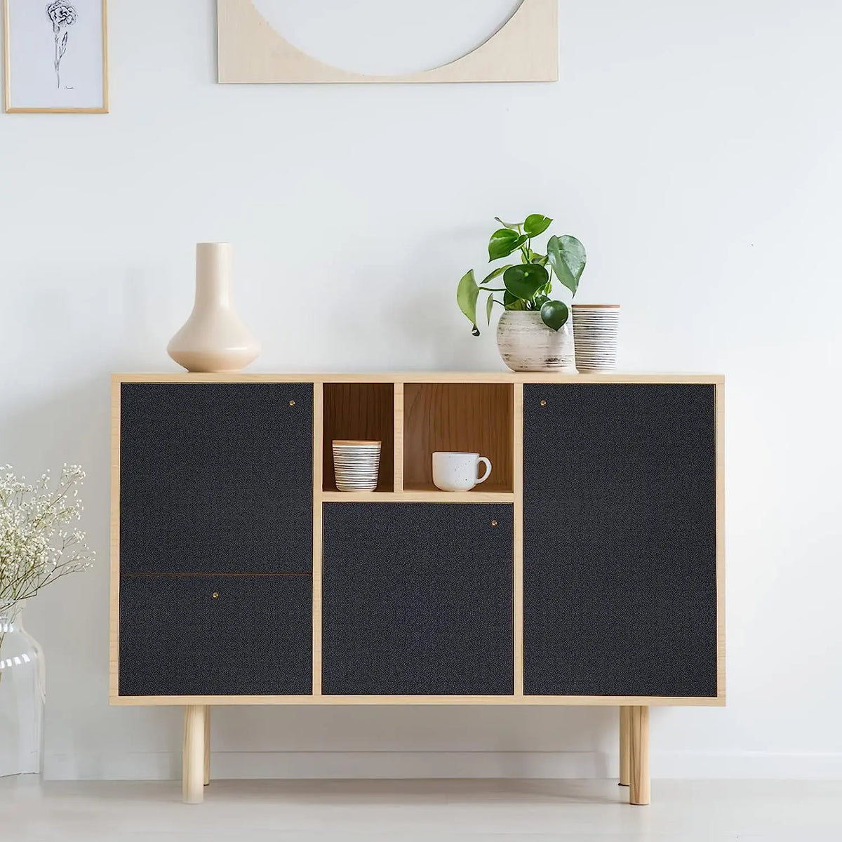 A wooden cabinet display featuring matte black self-adhesive vinyl wallpaper panels and small potted plants.