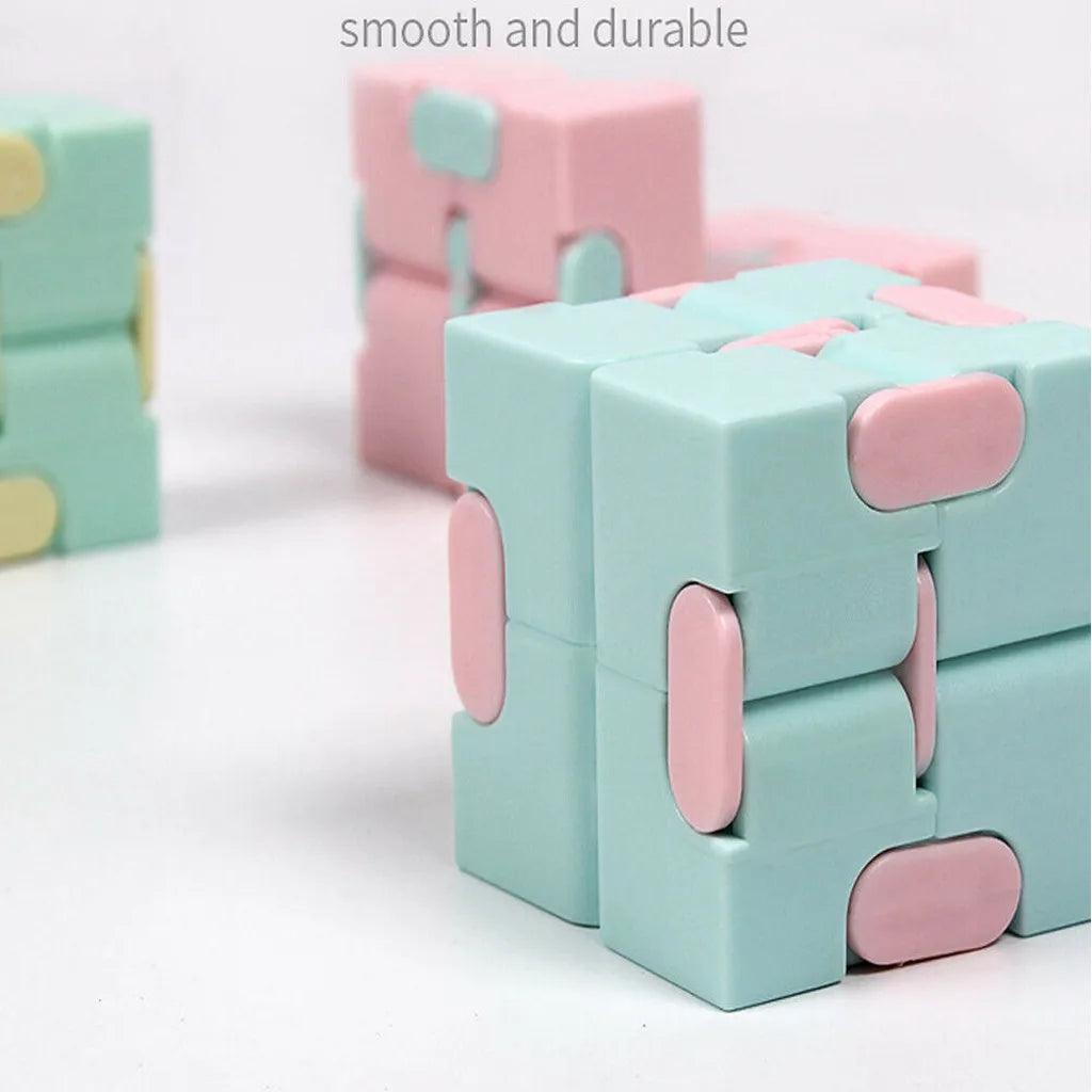 A close-up of a pastel pink and mint green Infinity Magic Cube fidget toy stacked on a white surface.