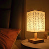 A Chinese style dimmable table lamp with a light linen shade sits on a wooden base on a dark surface.