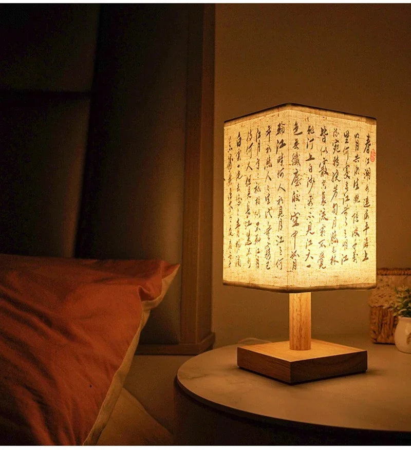 A Chinese style dimmable table lamp with a light linen shade sits on a wooden base on a dark surface.