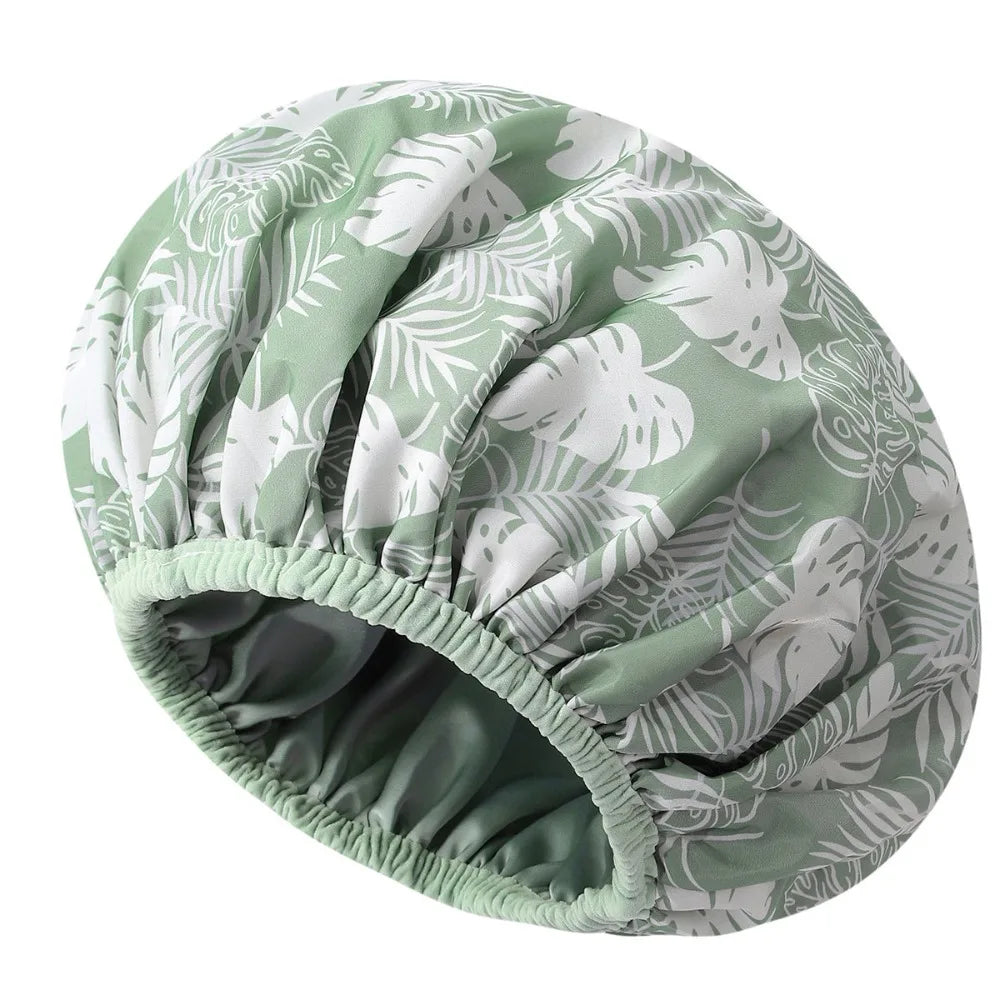 A large, satin-lined waterproof shower cap for hair protection with a green and white leaf pattern.