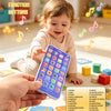 A toddler holds a colorful smartphone learning toy with various buttons and icons, demonstrating educational functions.