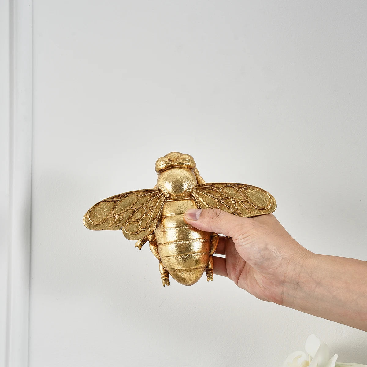 A hand is holding a golden bee-shaped resin wall decor against a white background.