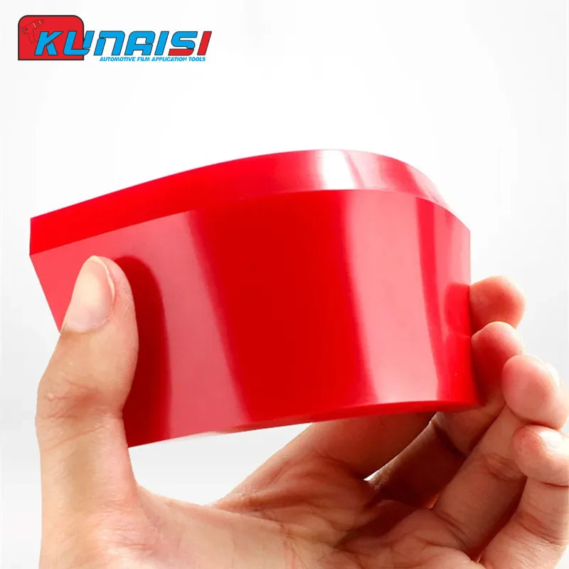 A hand is holding a bright red car windshield ice scraper and squeegee tool.