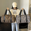 A woman holds a leopard print weekender tote bag with a shoe compartment in front of her.