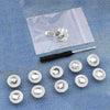 A collection of silver instant no-sew snap buttons laid out on a translucent plastic sheet.