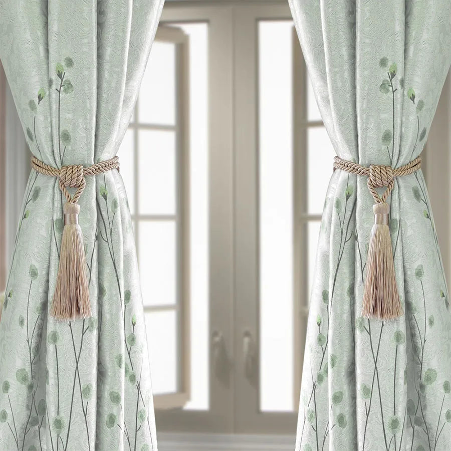 A pair of light green sheer curtains with floral patterns tied back by natural fiber tassels.
