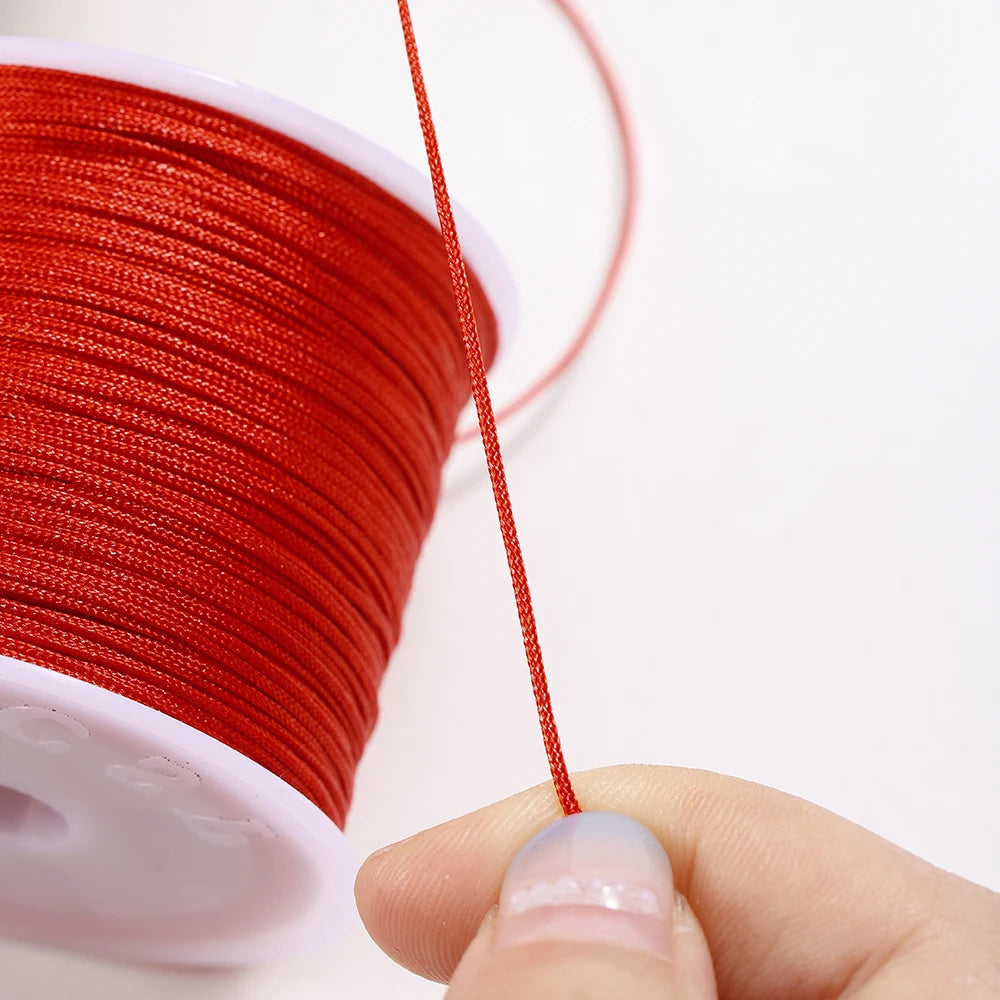 A spool of red nylon macramé cord is shown with a single strand being pulled out for jewelry making.