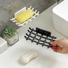 A hand is placing a light-colored soap bar onto a black wall-mounted soap dish with drainage holes.