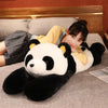 A woman is lying down on a sofa with a giant black and white panda plush toy resting beside her.