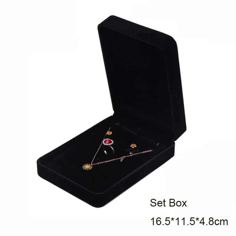 Black velvet jewelry storage box with a lid displaying a delicate gold necklace and earrings.