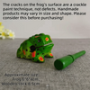 A handcrafted wooden frog percussion instrument with green body and black spots resting on a gray surface.