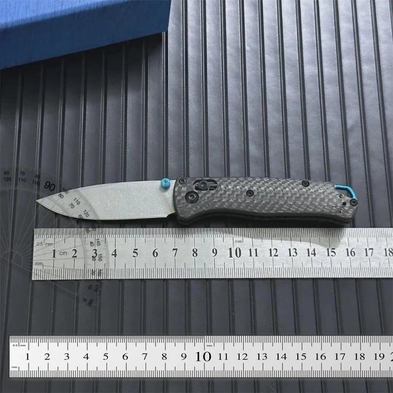 A carbon fiber folding knife with an axis lock is shown next to a ruler for scale.