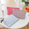 A collection of plaid makeup bags in pink, purple, and blue are displayed on a white table next to a lamp.