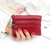 A red leather coin purse with a silver chain and zipper is held by a hand next to a cup and some papers.