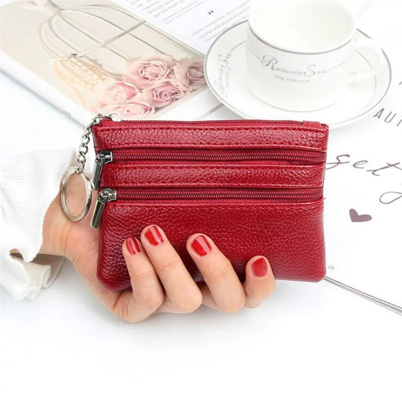 A red leather coin purse with a silver chain and zipper is held by a hand next to a cup and some papers.