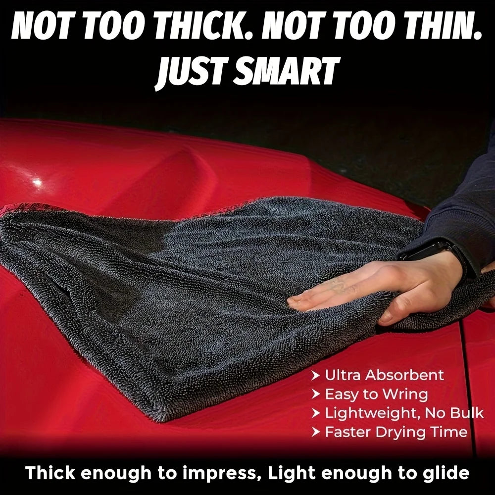 A dark gray microfiber drying towel is shown draped over a red vehicle surface.