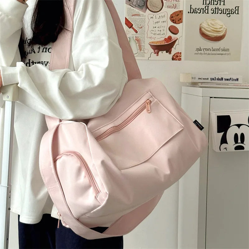 A pink canvas travel tote bag with a strap is being held by a person in a white shirt.
