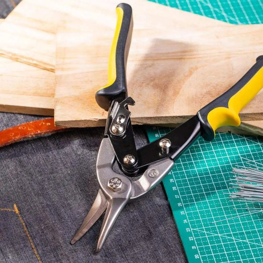 A pair of black and yellow heavy-duty aviation snips is shown resting on a wooden cutting board and a green grid mat.
