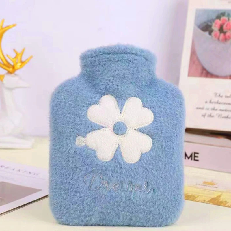 A light blue plush-covered hot water bottle with a white flower design and the word Dreams embroidered on it.