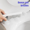 A hand is using a white brush with dense soft bristles in soapy water inside a toilet bowl.