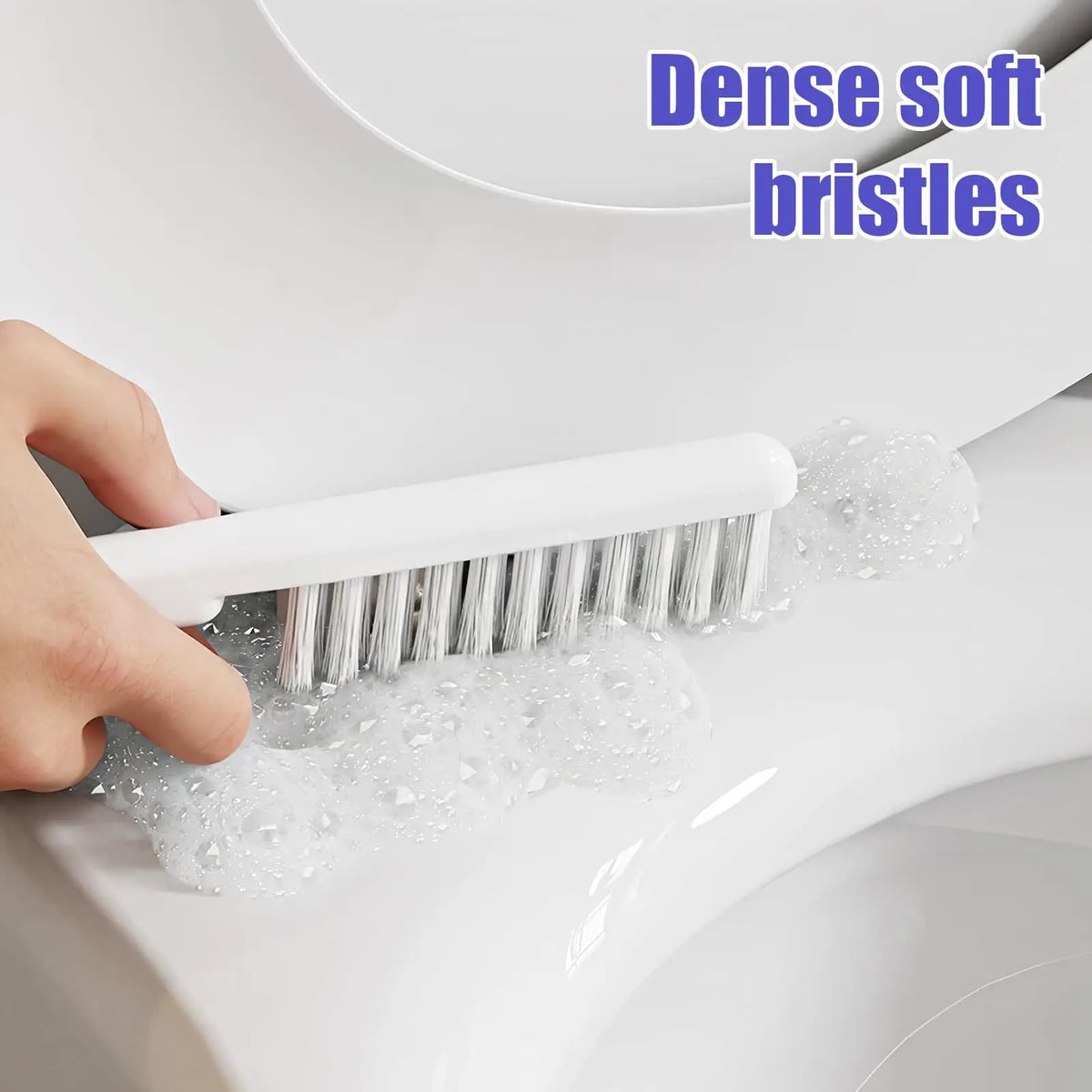 A hand is using a white brush with dense soft bristles in soapy water inside a toilet bowl.