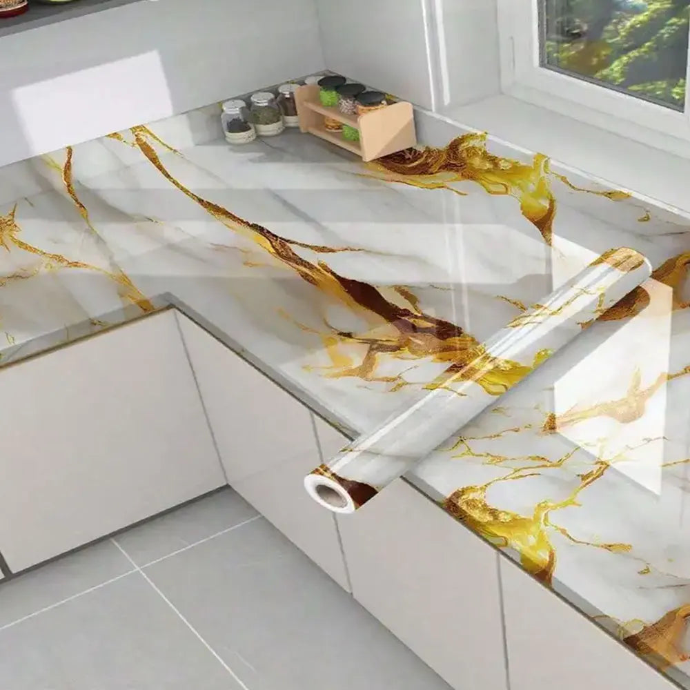 Roll of self-adhesive marble contact paper featuring gold and brown veining on a kitchen countertop