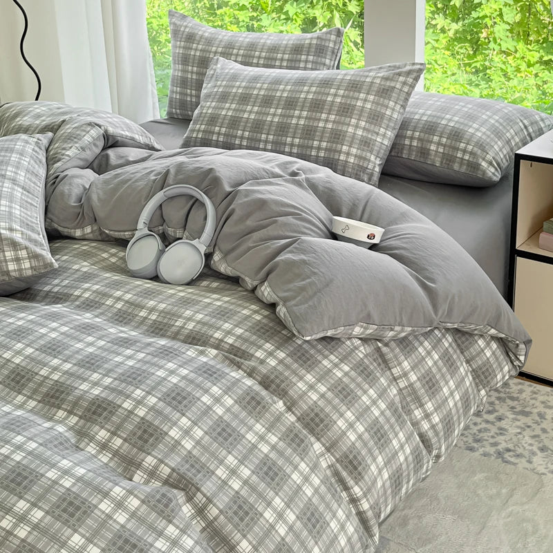 A gray plaid duvet cover set with two pillowcases and a matching pillow on a bed.
