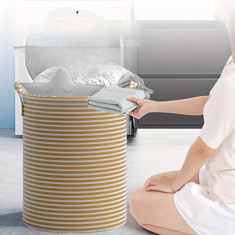 A person is holding a striped laundry basket with handles, featuring gold and white stripes, in a bright indoor setting.