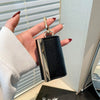 A hand holds a black and silver retractable keychain tote bag folded into a compact pouch.