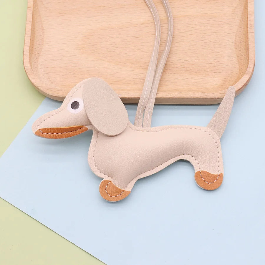 A light tan dachshund puppy keychain made of PU leather lying on a wooden cutting board.
