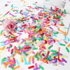 A pile of colorful confetti paper shreds scattered on a white surface next to a pink rose.