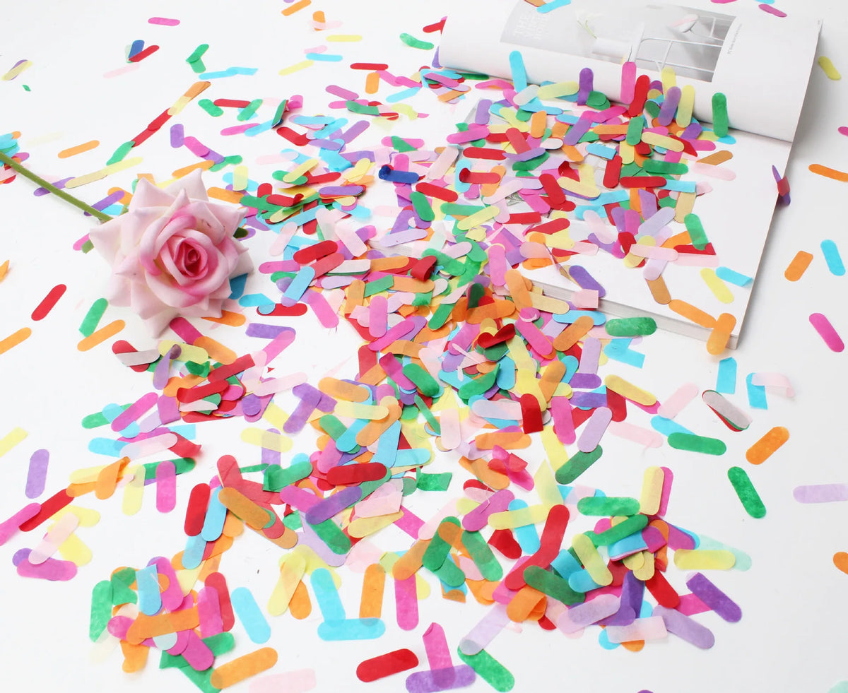 A pile of colorful confetti paper shreds scattered on a white surface next to a pink rose.