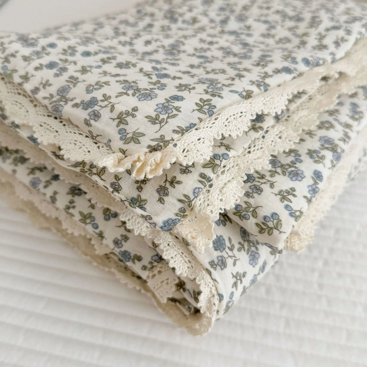 Folded floral muslin baby blanket with delicate lace trim in blue and white patterns
