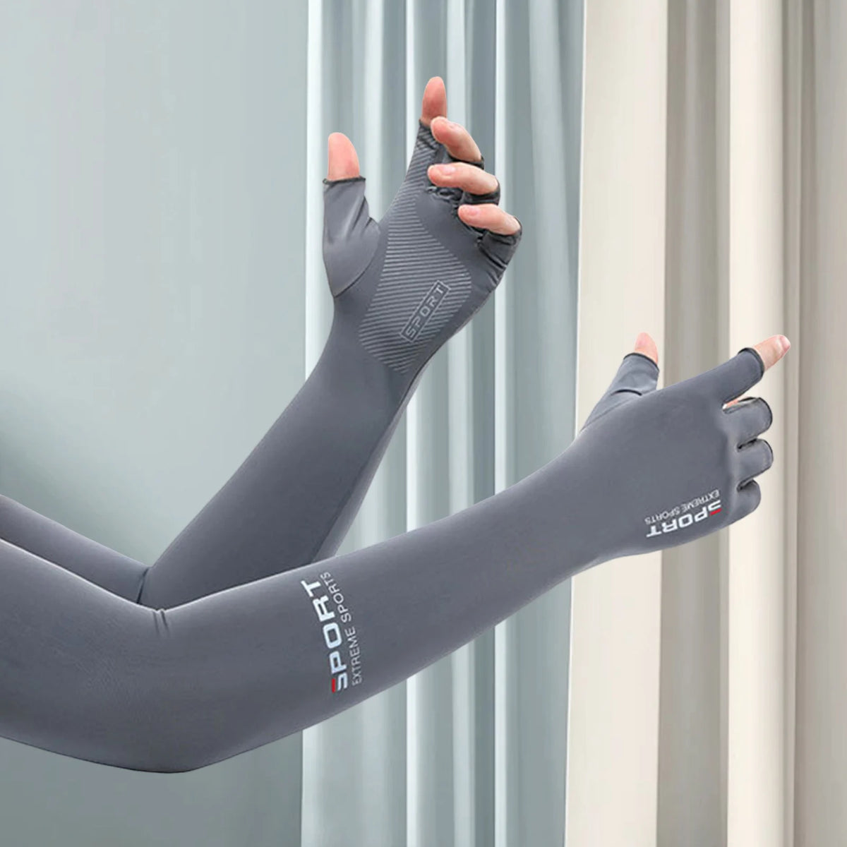 Gray sports arm sleeves being worn on an arm against a light gray curtain backdrop.