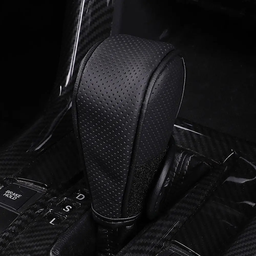 A close-up view of a black gear shift knob cover with a perforated texture, shown in a dark interior context.