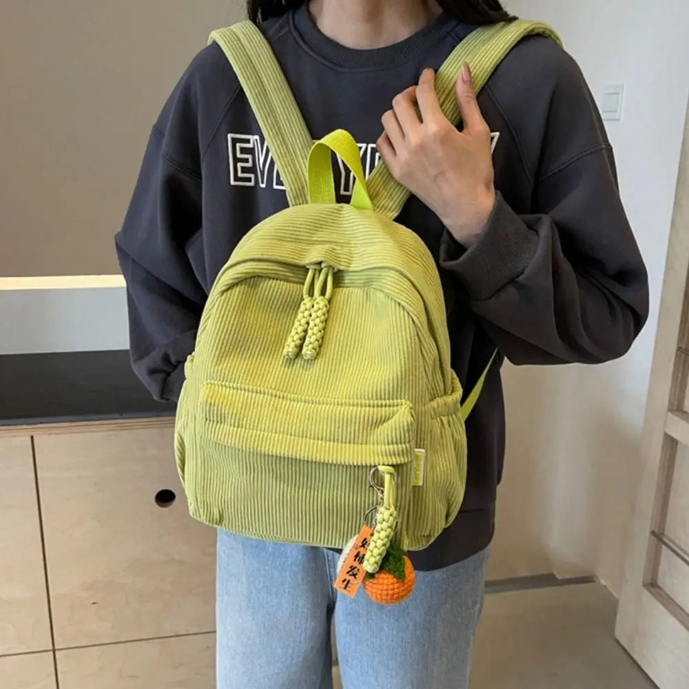 A person is wearing a lime green corduroy casual backpack over a dark sweatshirt.