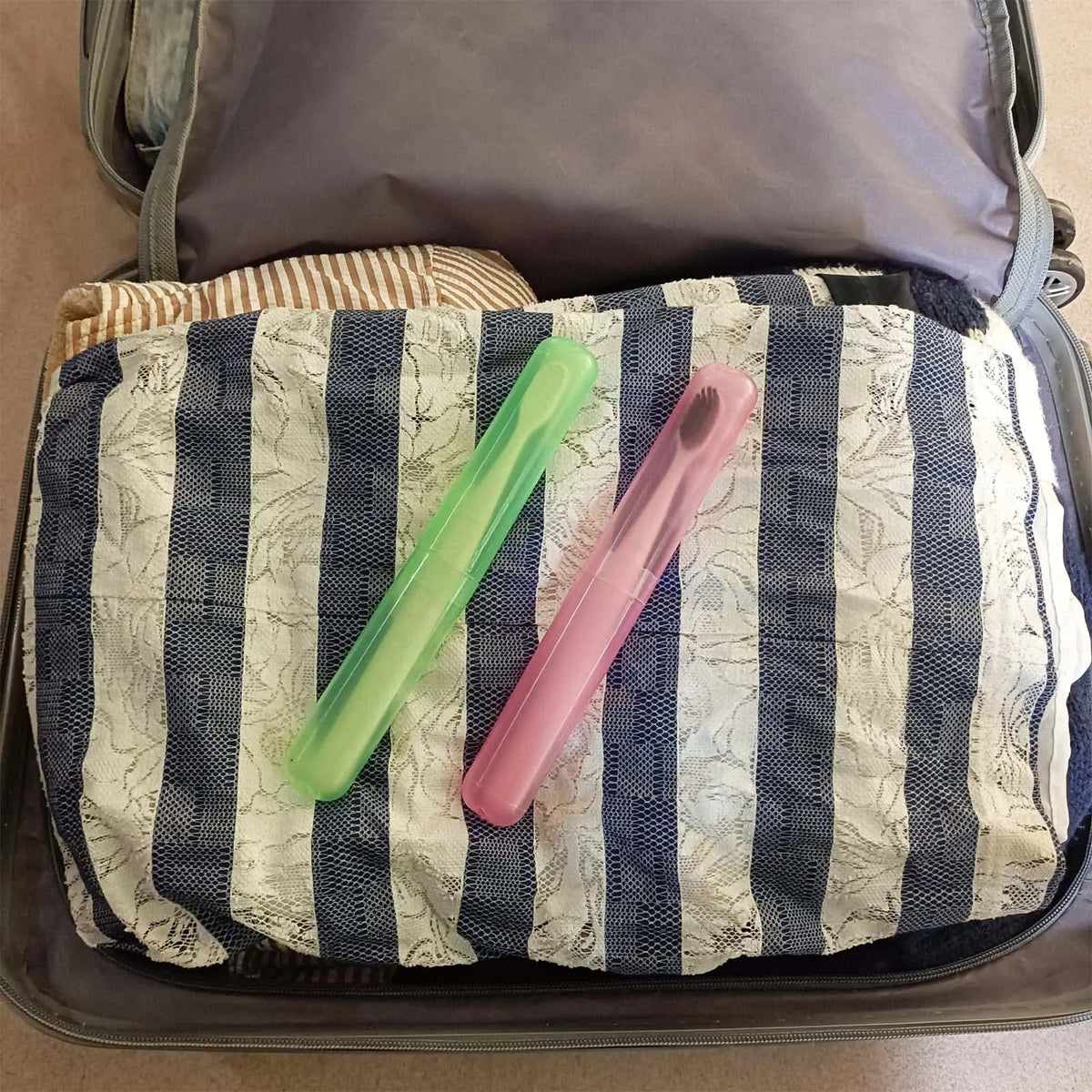A pink and green travel toothbrush case is shown inside a gray zippered pouch.