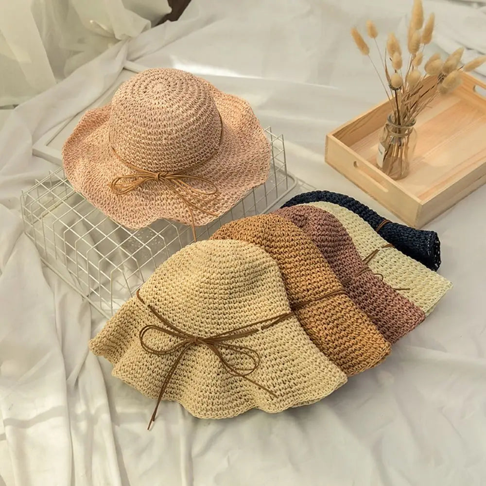 Colección de sombreros de paja tejidos en varios tonos naturales, exhibidos en una rejilla de vidrio sobre tela blanca.