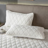 White quilted pillow protector with envelope closure resting on a gray headboard and white bedding.