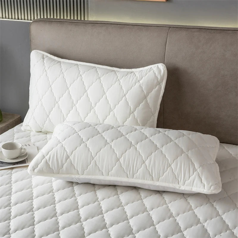 White quilted pillow protector with envelope closure resting on a gray headboard and white bedding.