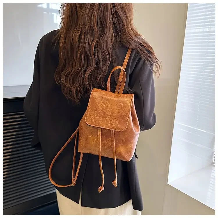 Petit sac à dos à cordon en cuir marron porté par une personne, vu de dos.