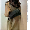 A woman models a beige trench coat and a black vintage leather crossbody bag with a flap closure.