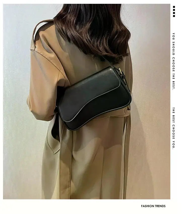 A woman models a beige trench coat and a black vintage leather crossbody bag with a flap closure.