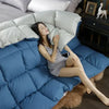A woman relaxing on a blue quilted comforter with white pillows and a white goose down comforter nearby.
