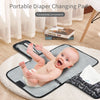 A portable foldable diaper changing pad is shown on a white rug with a baby lying on it.