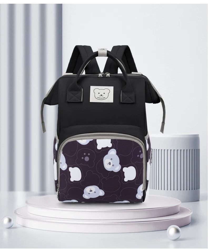 A black waterproof diaper backpack with a bear print pattern displayed on a white pedestal.